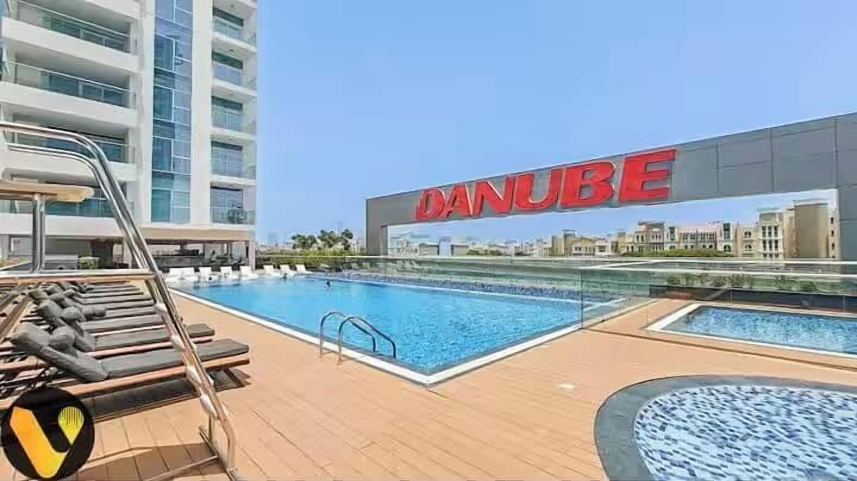 Zona de piscina con sillas de descanso y un edificio con la señalización 'DANUBE'.