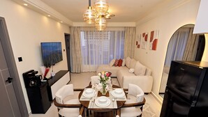 Uma área de refeições com uma mesa posta para quatro pessoas, um sofá, uma TV e um refrigerador.