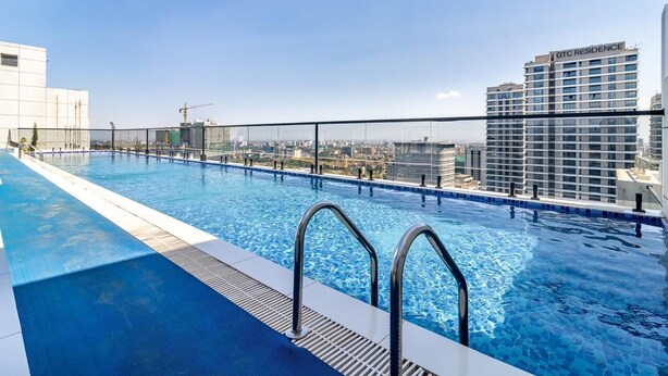 Uma piscina infinita no terraço com vista para a cidade, um edifício alto com a inscrição 'GTC RESIDENCE' e uma grua de construção ao fundo.