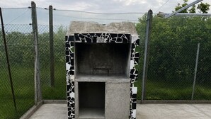A concrete outdoor grill with a mosaic pattern, surrounded by a chain-link fence and greenery. - Country house near the sea in a quiet area (Oliva)