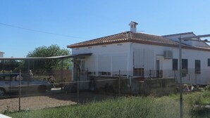 A white building with a tiled roof, a fenced yard, and a parked car. - Country house near the sea in a quiet area (Oliva)