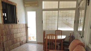 A living room with a sofa, a dining table with chairs, a tiled floor, a sliding glass door, and an air conditioning unit. - Country house near the sea in a quiet area (Oliva)