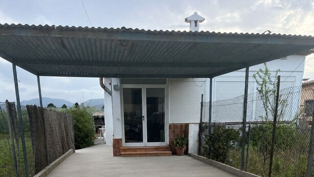 A covered patio area with a concrete floor, a white building with a glass door, and a metal roof. - Country house near the sea in a quiet area (Oliva)