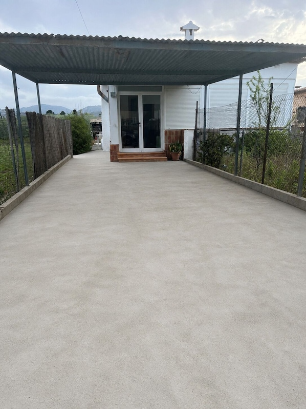 A covered patio area with a concrete floor, a white building with a glass door, and a metal roof.