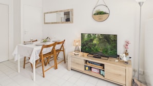 Spiseområde med et bord dækket til to personer, et fjernsyn på et træfagot og en hængende plante.