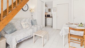 En stue med en trætrap, en hvid sofa, et sofabord og et spiseområde med et bord dækket til to.