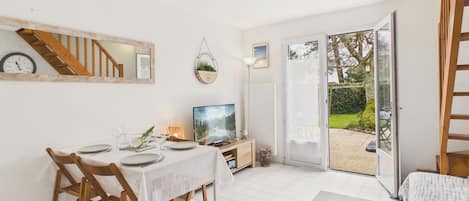 Een eetruimte met een tafel voor vier personen, een televisie en een schuifdeur naar een tuin.