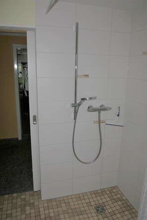 Ein Badezimmer mit Dusche, gefliesten Wänden und einer Tür zu einem anderen Raum.