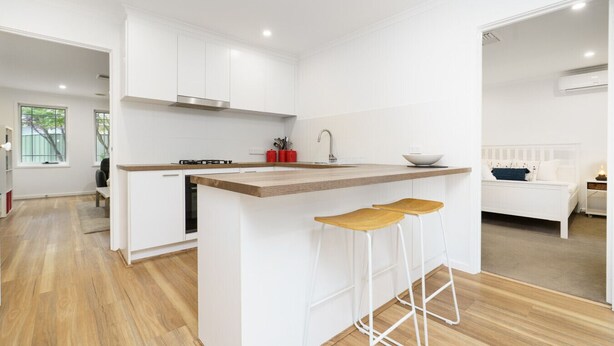A modern kitchen with white cabinetry, a wooden countertop, and two bar stools.