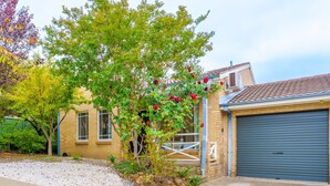 A residential property with a garage, a tree with red flowers, and a gravel driveway.