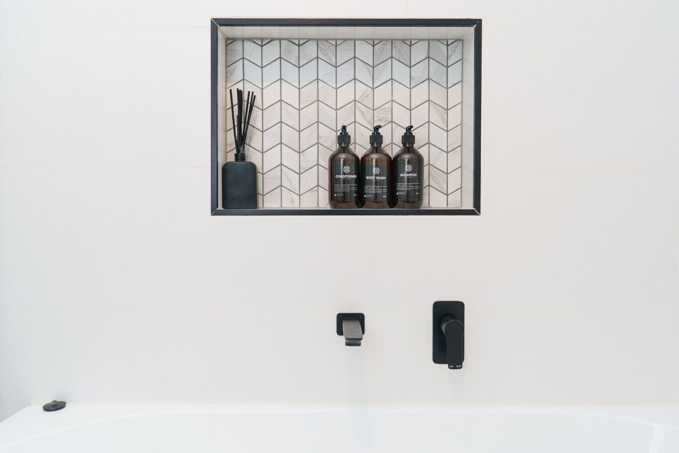 A bathroom with a white sink, a black soap dispenser, and a bottle of shampoo.