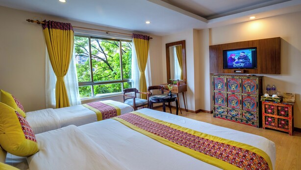 A hotel room with two beds, a TV, a desk, and a cabinet with decorative items. - Hotel Central Prime (Kathmandu)