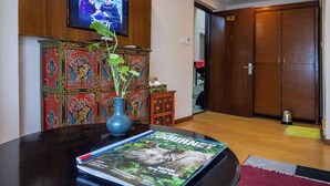 A living room with a television, a magazine on a table, a decorative cabinet, and a wooden door. - Hotel Central Prime (Kathmandu)
