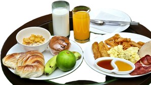 A breakfast tray with croissants, a muffin, a banana, a lime, scrambled eggs, bacon, hash browns, and two glasses of orange juice. - Hotel Central Prime (Kathmandu)