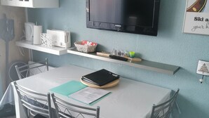 Ett modernt kök med en platt-TV, vita skåp, ett matbord med stolar och en blå accentv ägg.
