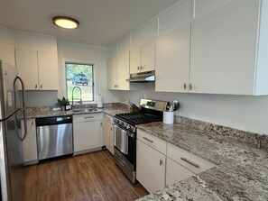 A modern kitchen with stainless steel appliances, white cabinetry, and a granite countertop. - Updated Townhome Near Mount Snow & Hermitage Club I Fireplace, Golf Course Views (Wilmington)