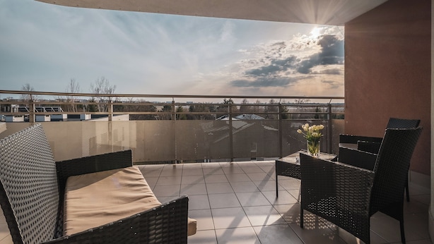Un balcón con mesa y sillas, un jarrón de flores y vistas al cielo y edificios lejanos.