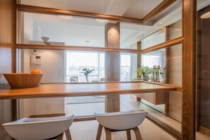 Een moderne keuken met een houten aanrecht, twee witte stoelen en uitzicht op de stad door grote ramen.