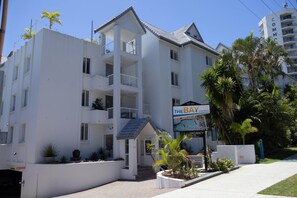 A multi-story building with balconies, a sign for 'The Bay Apartments,' and surrounding palm trees. - Rainbow Sky Terrace - Ocean Views & Private Spa (Coolangatta)