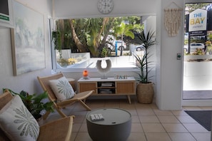 Ein modernes Wohnzimmer mit großem Fenster, einer Uhr, einem Sofa, einem Couchtisch und einem Schild mit der Aufschrift 'The Bay Apartments'.
