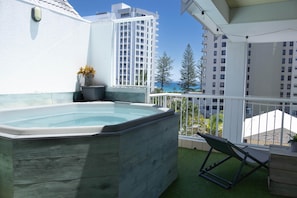 Eine Dachterrasse mit Whirlpool, Liegestuhl und Blick auf das Meer und Gebäude.