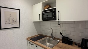 A kitchen with white cabinets, a stainless steel sink, a black microwave, and a framed picture on the wall. - Balcony apartment | near the lake | climate | near Bremen (Ganderkesee)