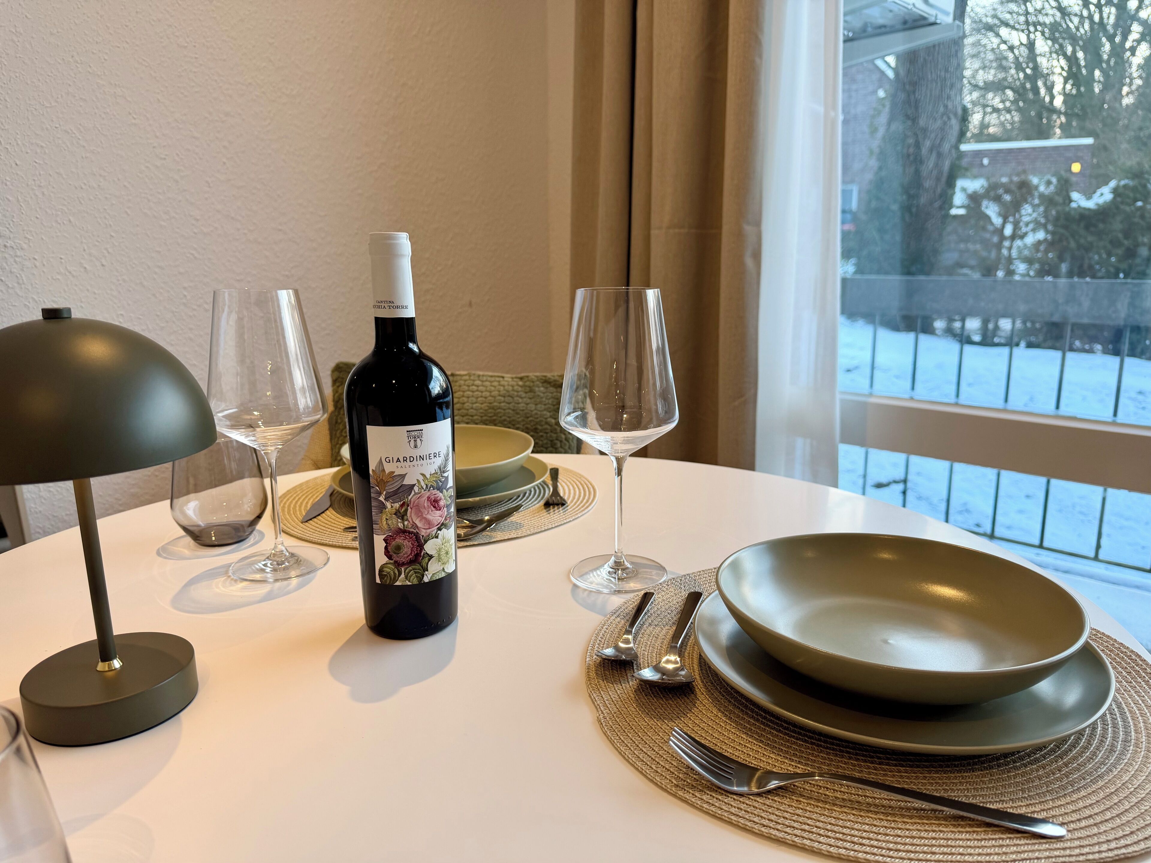 Een eettafel met een fles wijn, glazen, borden en bestek.