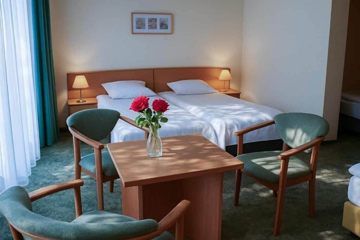 Ein Hotelzimmer mit einem Bett, zwei Nachttischen mit Lampen, einem kleinen Tisch mit Stühlen und einer Vase mit Blumen.