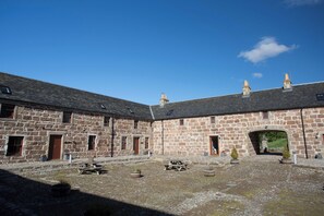 A stone building with multiple rooms, a courtyard with a picnic table, and a covered entrance. - Simmental Cottage (Daviot)