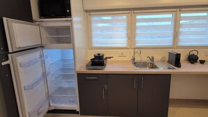 Eine kompakte Küche mit integriertem Mikrowellenherd, Spüle und einem Fenster mit Jalousien.