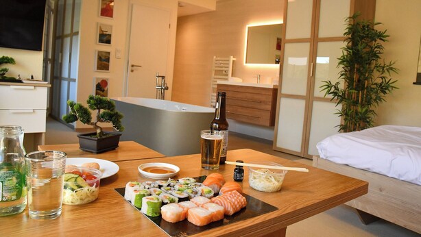 Ein Esstisch mit Sushi, Getränken und einer Flasche in einem modernen Hotelzimmer.