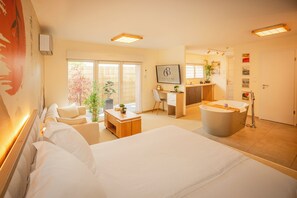 Quarto de hotel com cama, escrivaninha, poltrona, banheira e vista para o exterior.