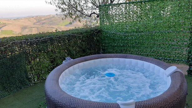 Ein Whirlpool mit Bedienfeld, umgeben von einer Hecke und Blick auf die Landschaft.