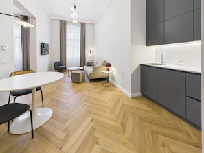 A modern hotel room with a herringbone wood floor, a round dining table, a sofa, a TV, and a kitchenette. - Griselini Boutique Suites (Timișoara)
