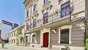 Un edificio con puerta roja, varias ventanas y un balcón con barandilla decorativa.