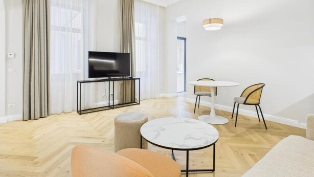 Una sala de estar moderna con un televisor de pantalla plana, una mesa de centro redonda, un sofá, una mesa de comedor con sillas y una lámpara en el techo.