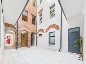 A courtyard with a white tiled floor, brick arches, and a modern building with a dark door. - Griselini Boutique Suites (Timișoara)