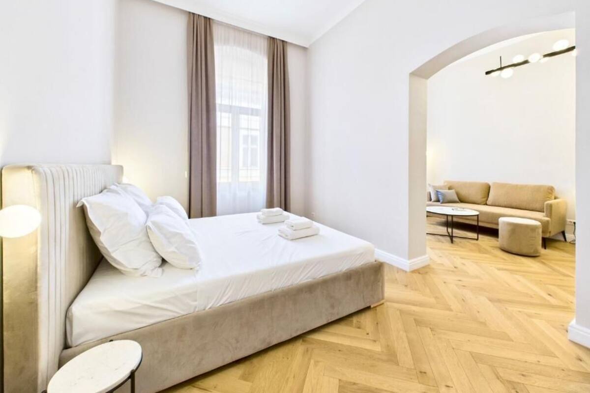 A modern hotel room with a bed, a round table, a sofa, and a large window with curtains.