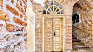 Un edificio rústico de ladrillo con puerta de madera, pared de piedra y escalera que conduce a un arco.