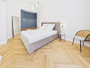 A modern bedroom with a large bed, a bedside table, a chair, and a mirror. - Griselini Boutique Suites (Timișoara)