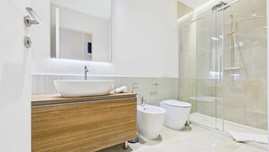 A modern bathroom with a wooden vanity, a large mirror, a glass shower enclosure, and a white sink. - Griselini Boutique Suites (Timișoara)