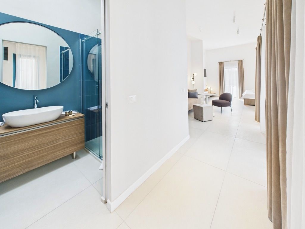 A modern bathroom with a large oval mirror, a white sink, and a wooden vanity.