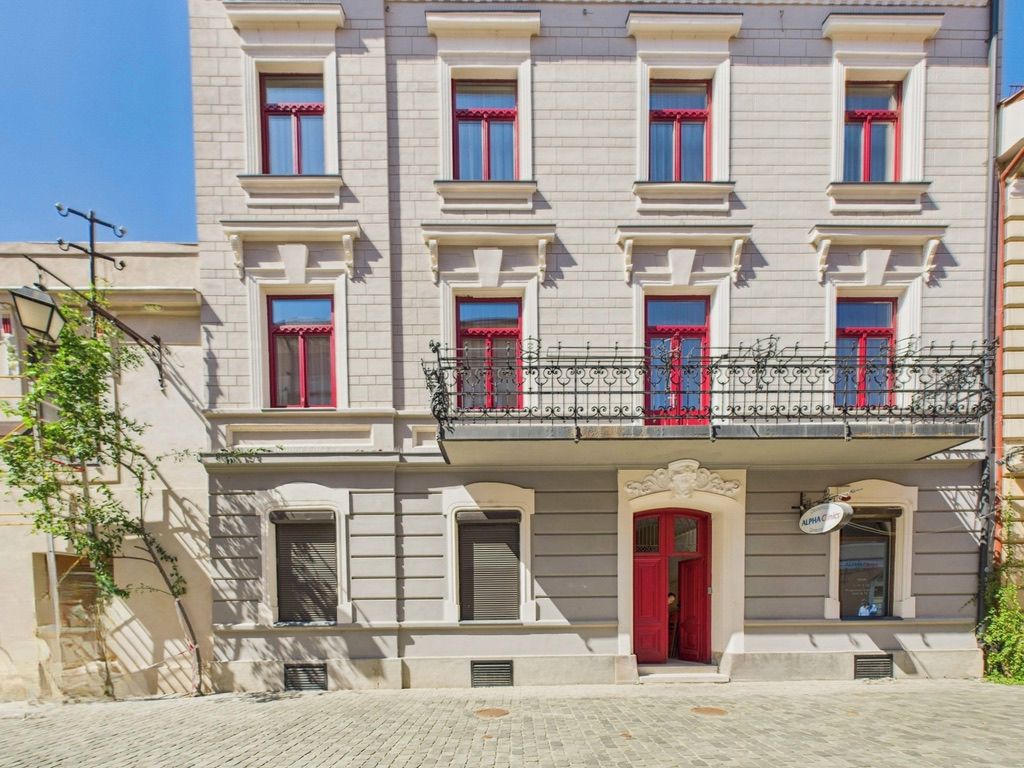 Een meerlaags gebouw met een balkon, rode deuren en een bord waarop een bedrijf wordt aangeduid.