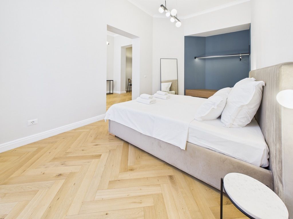 A modern hotel room with a large bed, a bedside table, and a mirror.