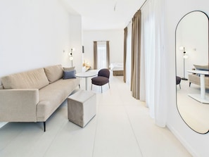 A modern hotel room with a sofa, a round table, a chair, a small ottoman, and a large mirror. - Griselini Boutique Suites (Timișoara)