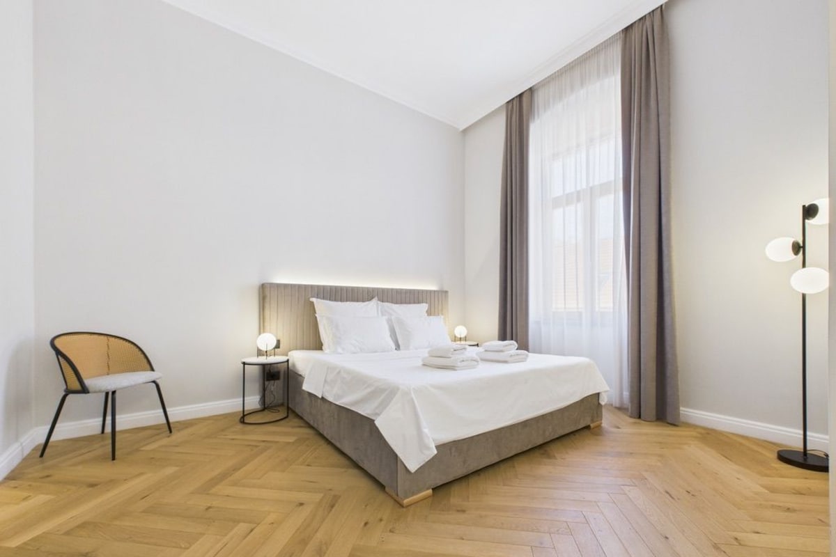Egy modern hálószoba, amelyben egy nagy ágy, egy éjjeliszekrény lámpával, egy szék és egy állólámpa található.