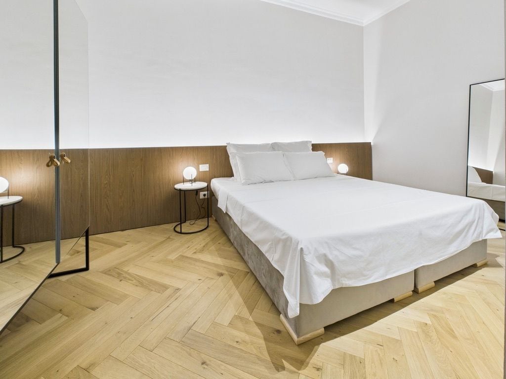 Een moderne slaapkamer met een groot bed, nachtkastjes en een spiegel.