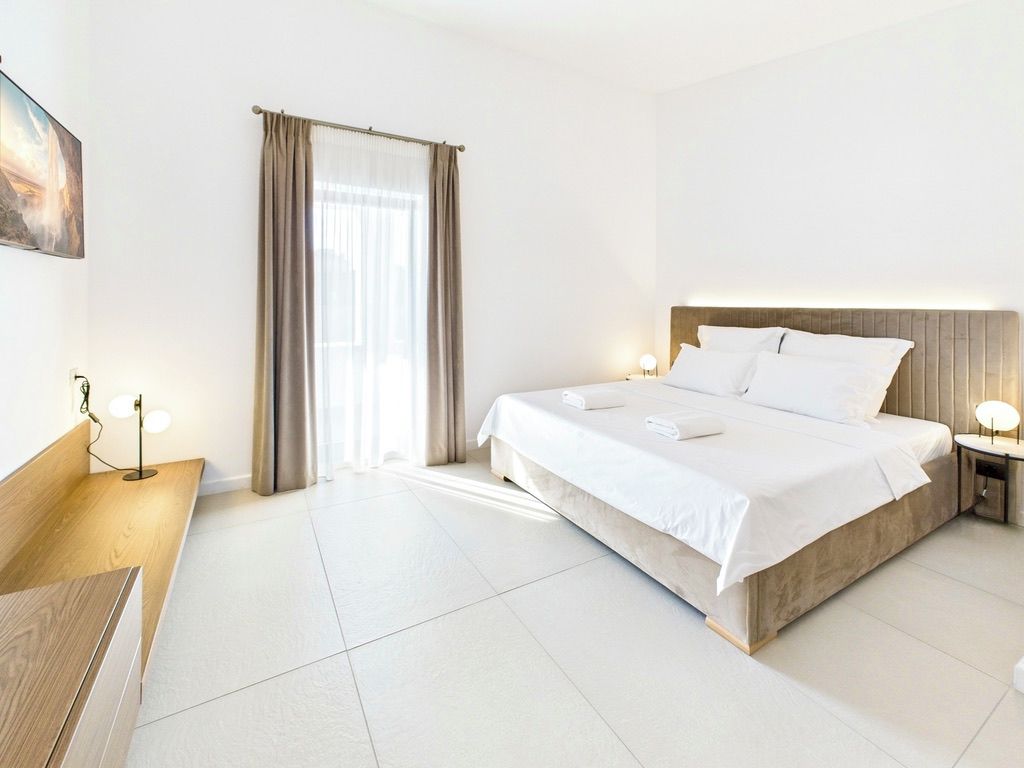 Habitación de hotel con cama, mesita de noche, lámpara y vista al exterior.