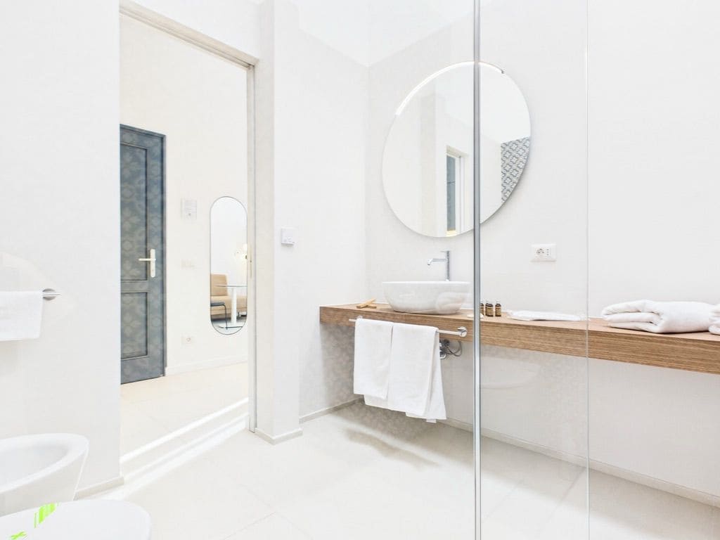 Un baño moderno con separador de vidrio, espejo redondo, tocador de madera y lavamanos blanco.