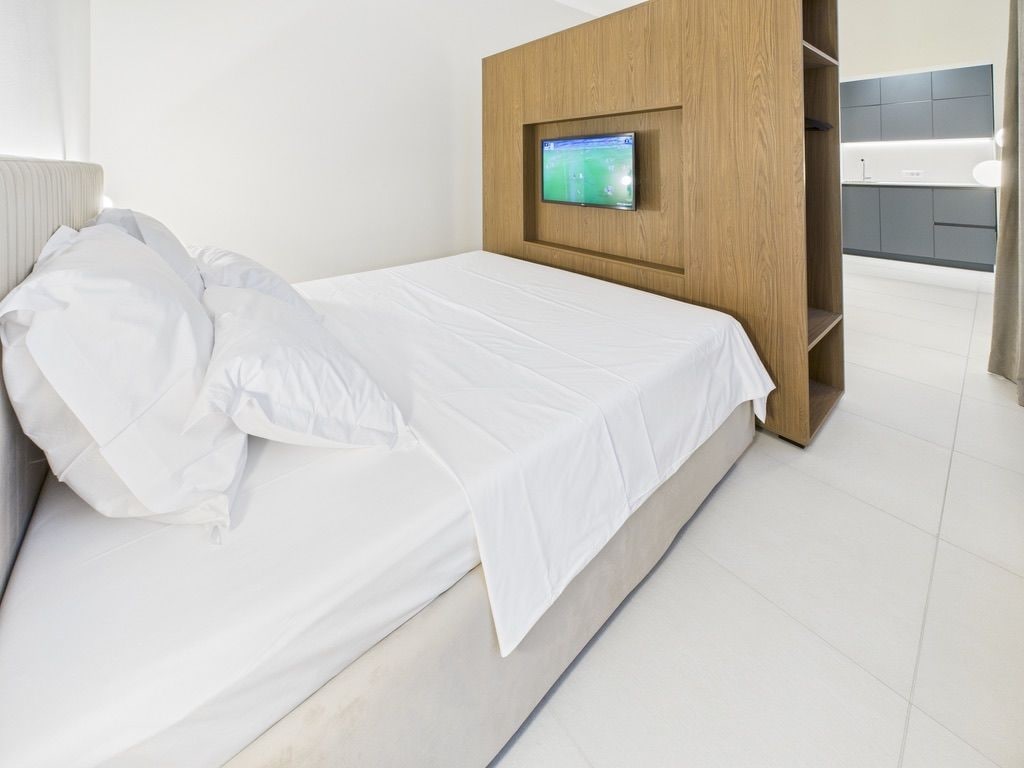 Een moderne slaapkamer met een bed, een televisie bevestigd aan het hoofdeinde en uitzicht op een badkamer.